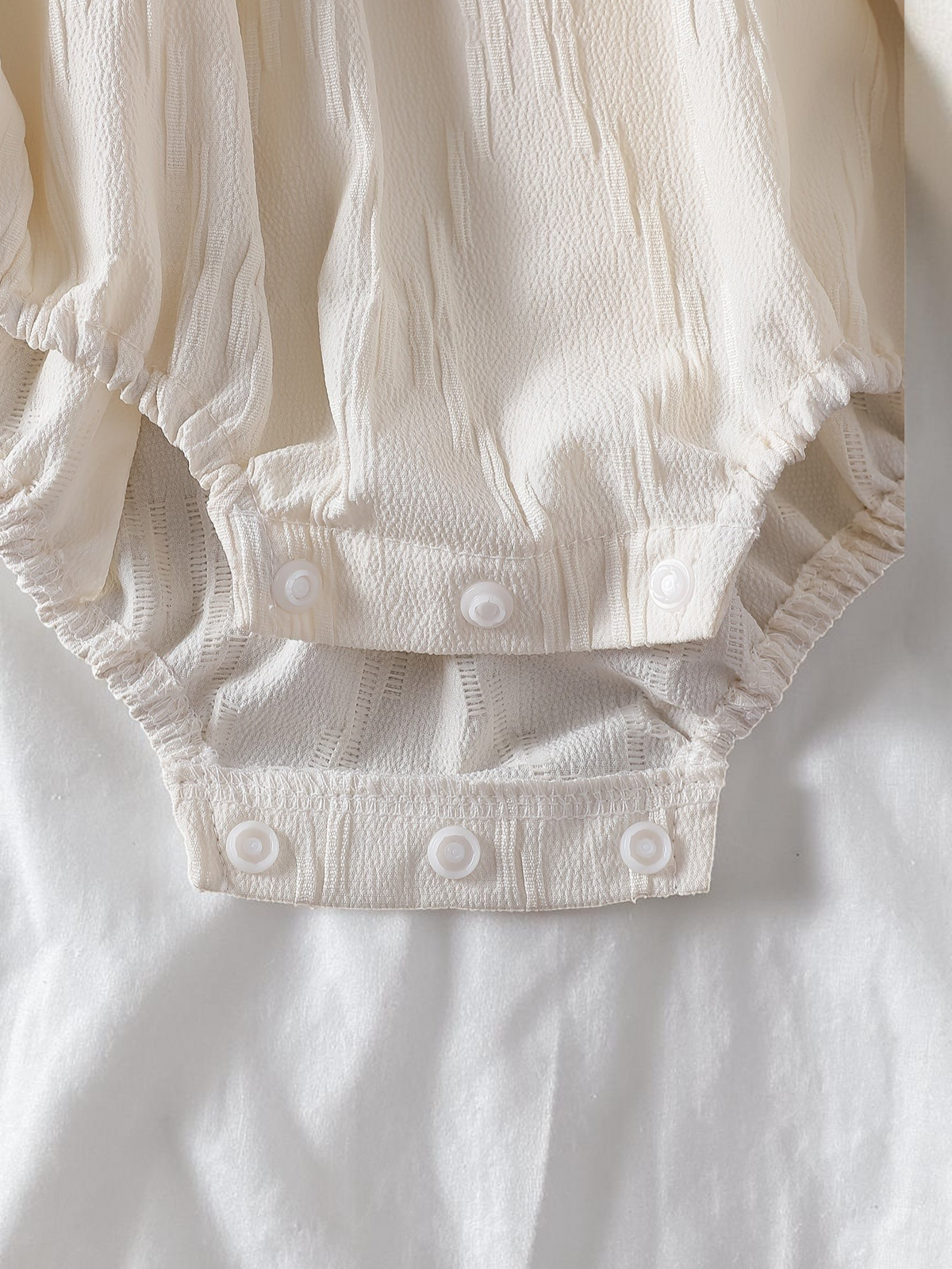 Détail de l'entrejambe à boutons-pression d'une combinaison Le Cocon d'Or pour bébé fille en polyester blanc texturé