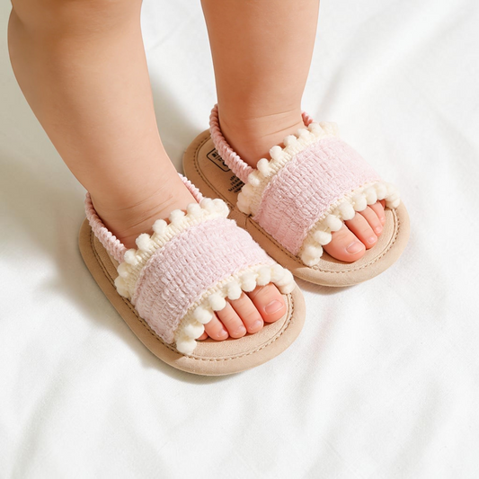 Sandales Le Cocon d'Or pour bébé en tissu rose pâle avec détails pompons blancs, style décontracté et confortable.
