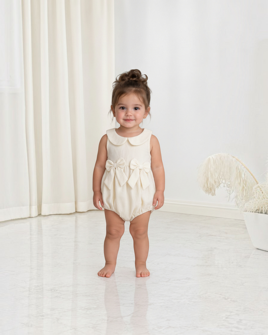 Petite fille portant une combinaison Le Cocon d'Or beige en polyester avec col claudine et nœuds décoratifs