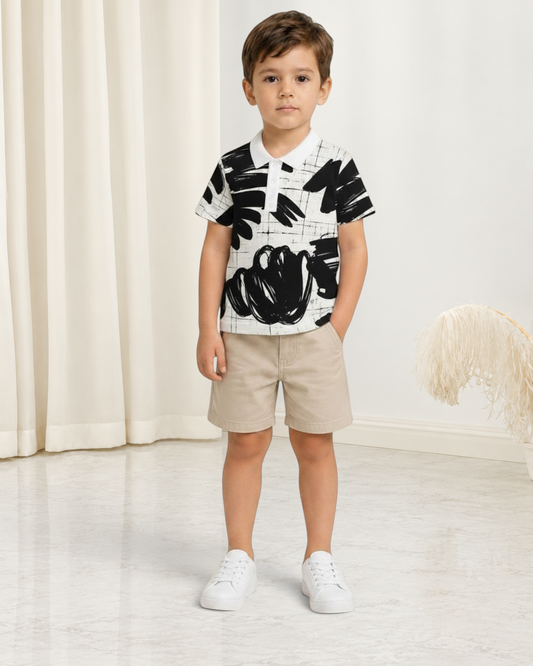 Jeune garçon portant un polo Le Cocon d'Or à motif abstrait noir et blanc avec col classique et short beige