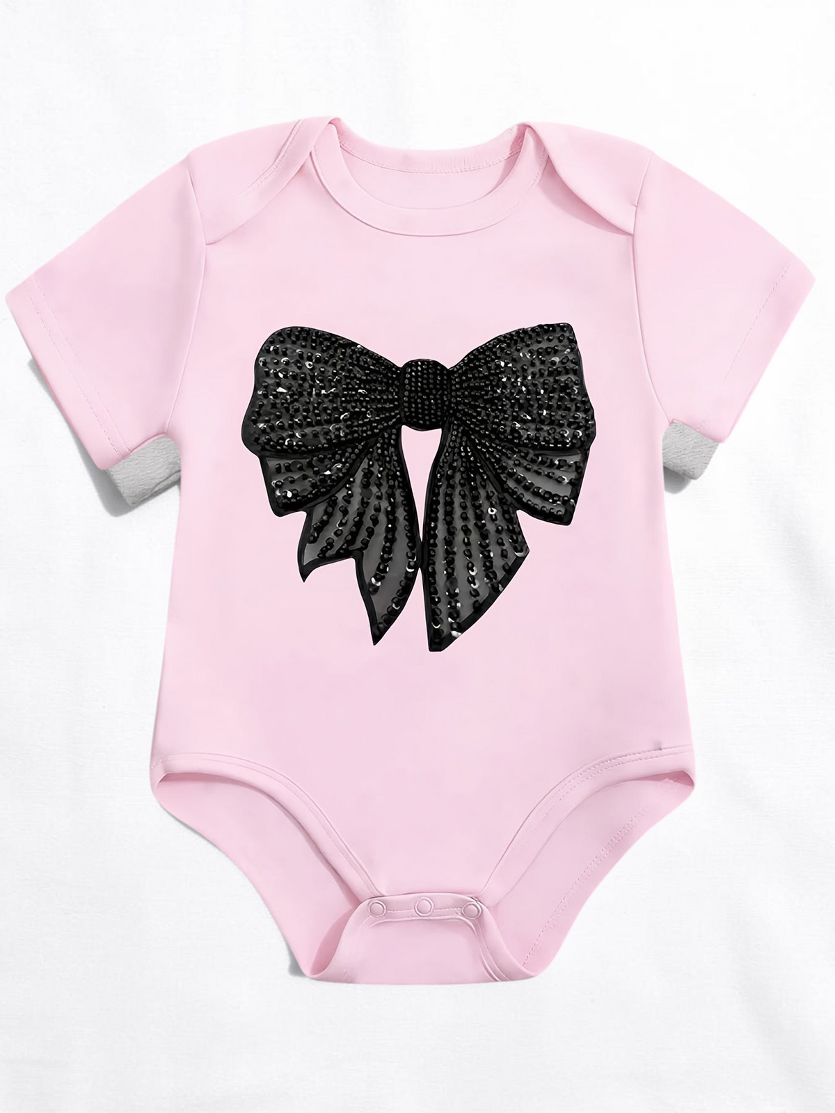 Grenouillère Le Cocon d'Or rose en coton pour bébé fille avec un grand nœud noir à paillettes imprimé sur le devant