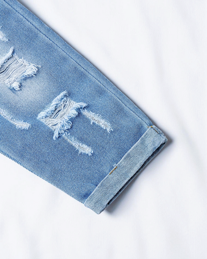 Gros plan sur une jambe de pantalon en jean bleu clair Le Cocon d'Or avec détails déchirés et ourlet retroussé