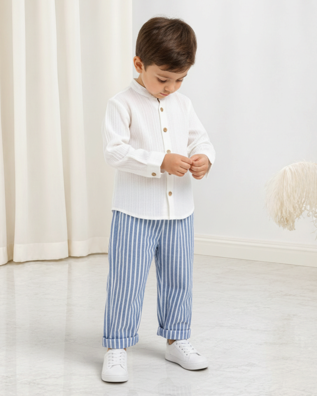 Jeune garçon portant un ensemble Le Cocon d'Or avec chemise blanche à boutons et pantalon rayé bleu et blanc