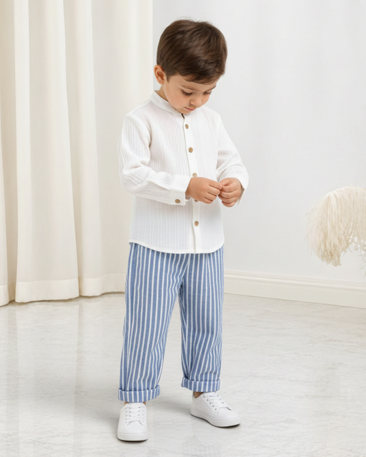 Jeune garçon portant un ensemble Le Cocon d'Or avec chemise blanche à boutons et pantalon rayé bleu et blanc