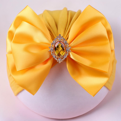 Chapeau turban jaune Le Cocon d'Or pour bébé avec un grand nœud en satin et une broche centrale en strass brillant