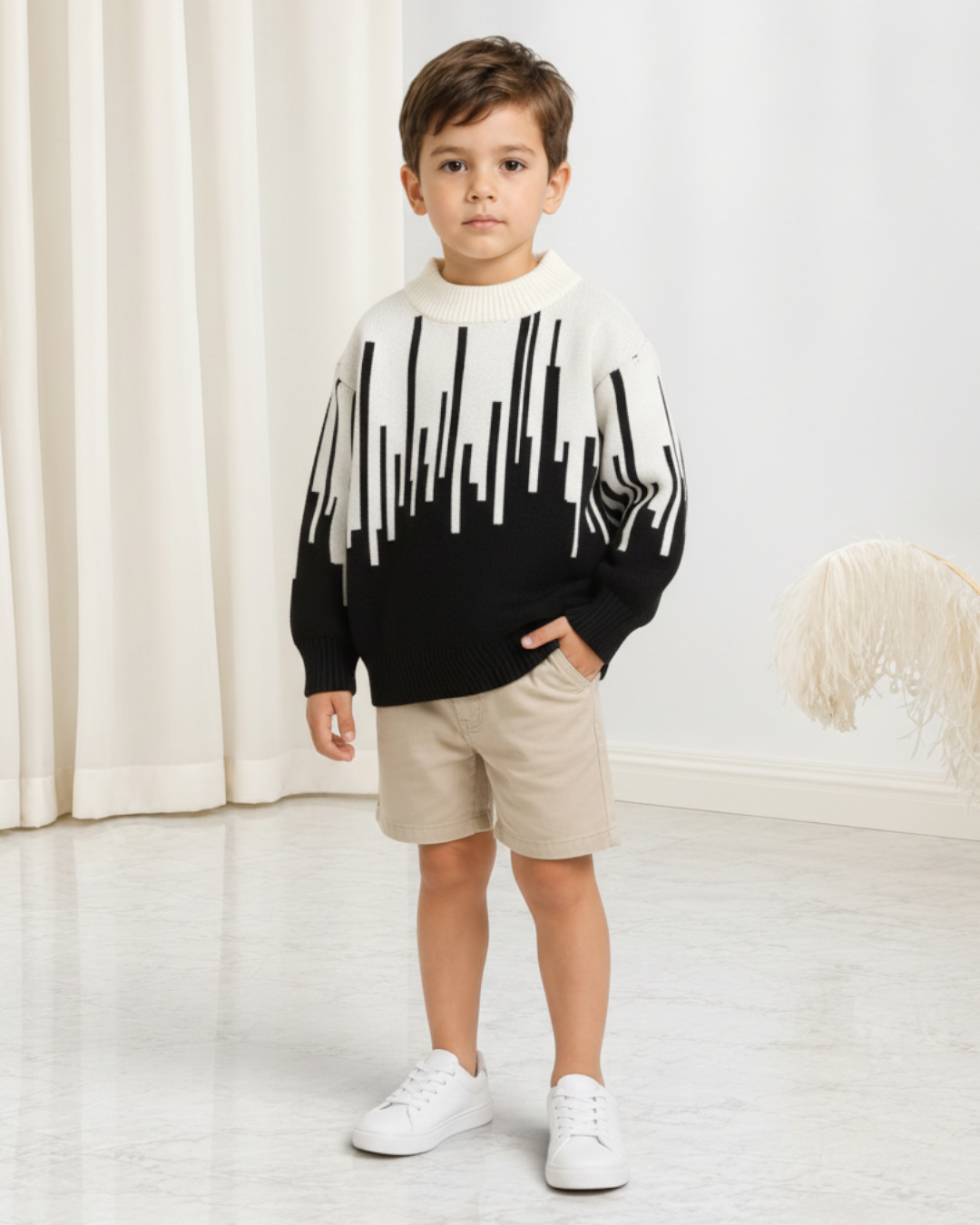 Jeune garçon portant un pull en maille Le Cocon d'Or noir et blanc à motif abstrait avec col rond et manches longues.