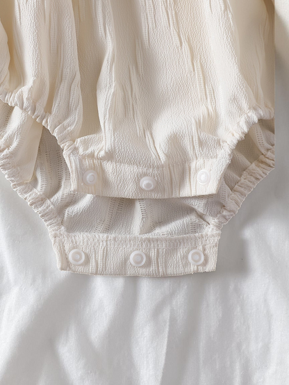 Détail de l'entrejambe à boutons-pression d'une combinaison Le Cocon d'Or pour bébé fille en polyester blanc texturé