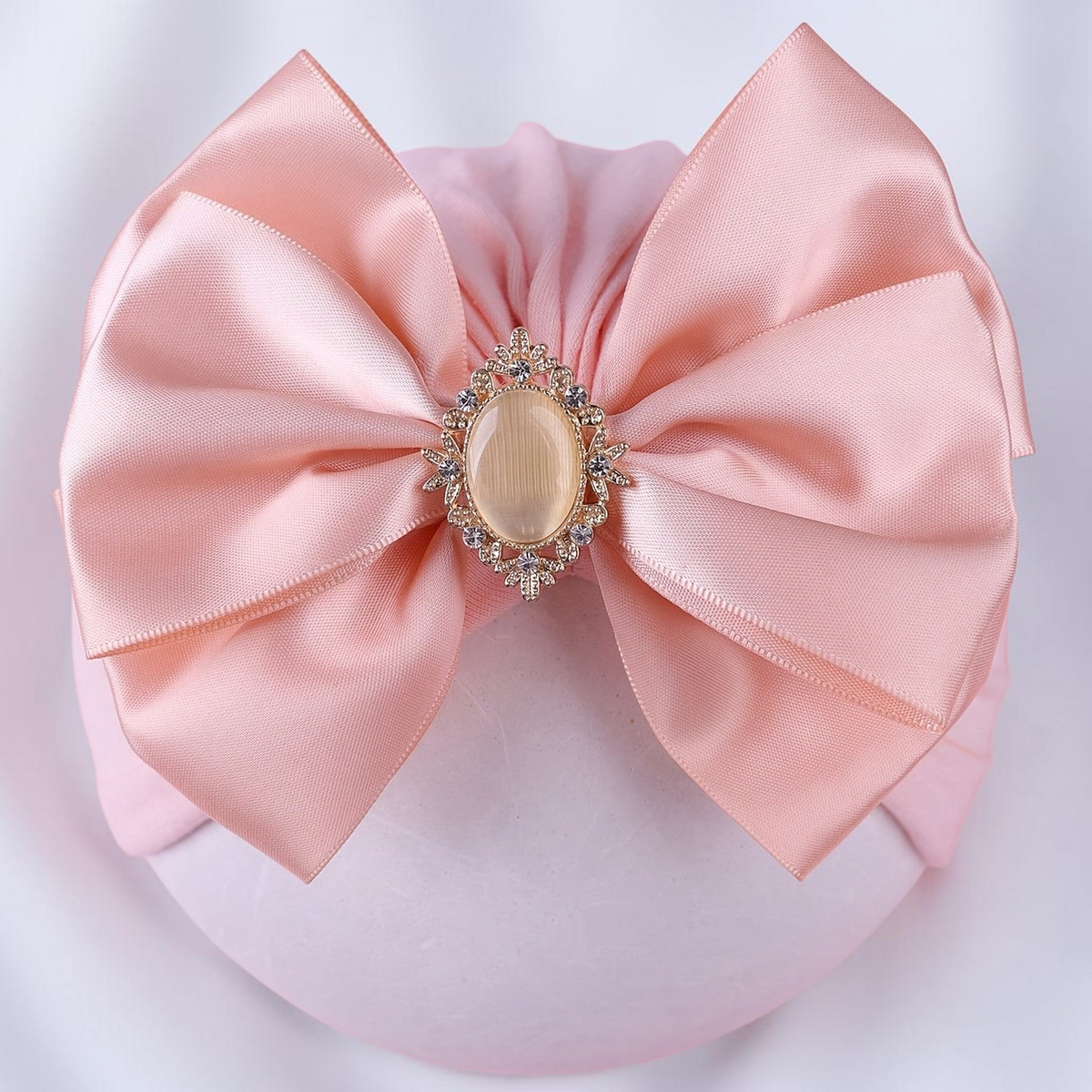 Bonnet bébé Le Cocon d'Or rose en polyester avec un grand nœud en satin et une broche centrale ornée de strass