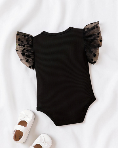 Combinaison Le Cocon d'Or pour bébé fille noire en maille avec manches en dentelle à pois sur fond en bois