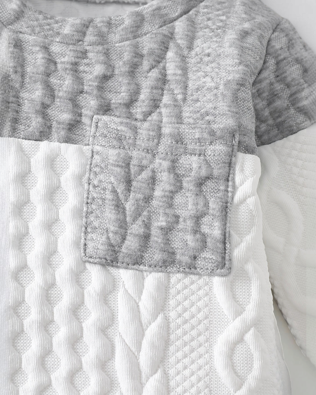 Gros plan sur le haut tricoté Le Cocon d'Or pour bébé garçon, en maille texturée gris et blanc avec poche poitrine.