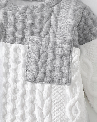 Gros plan sur le haut tricoté Le Cocon d'Or pour bébé garçon, en maille texturée gris et blanc avec poche poitrine.