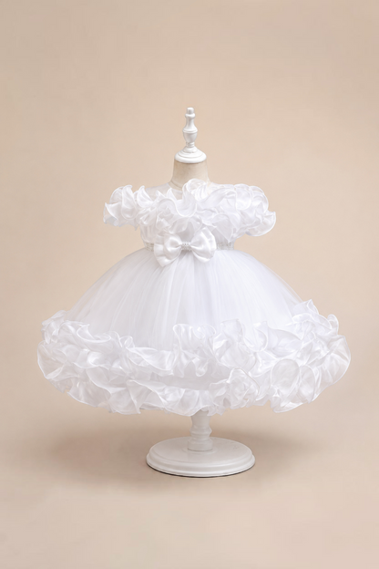Robe de cérémonie blanche Le Cocon d'Or pour bébé avec volants, perles et nœud décoratif sur un mannequin