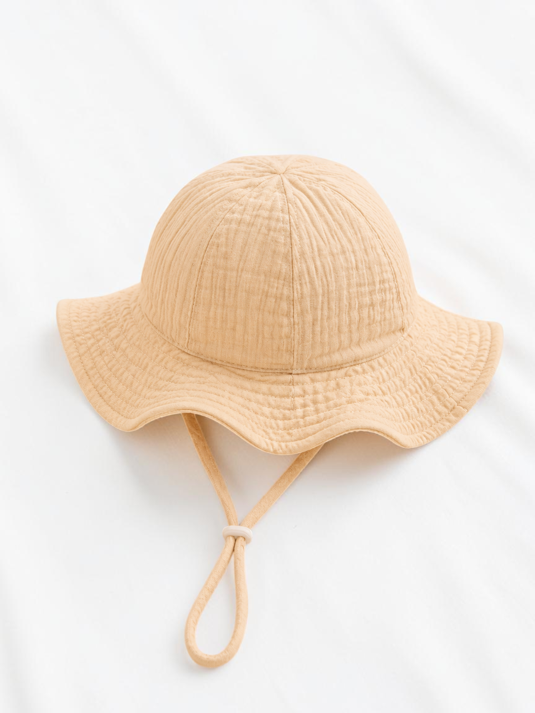 Bob pour bébé Le Cocon d'Or en coton beige texturé avec cordon de serrage, idéal pour le printemps et l'été.