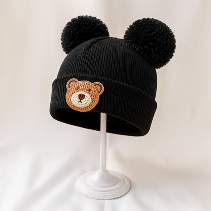 Bonnet noir en tricot Le Cocon d'Or avec pompons et motif ours pour bébé, idéal pour l'automne et l'hiver.