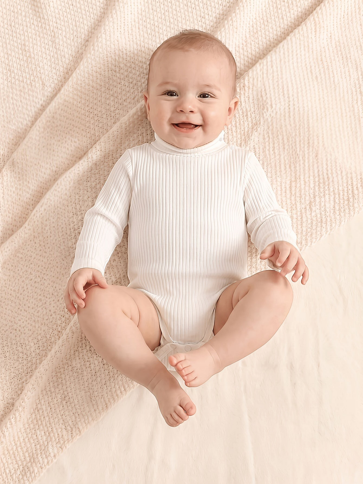 Bébé souriant portant une barboteuse Le Cocon d'Or blanche à col roulé en maille côtelée douce et manches longues