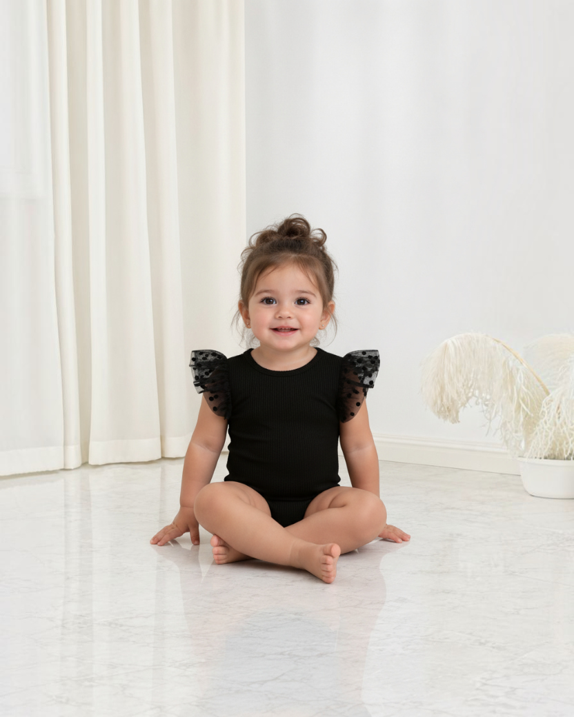 Bébé fille portant une combinaison noire Le Cocon d'Or avec manches en dentelle à pois, style décontracté et élégant