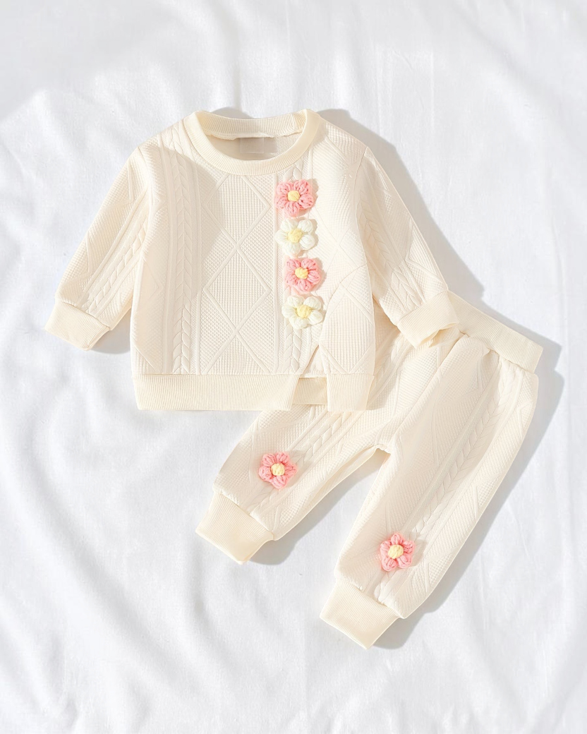 Ensemble Le Cocon d'Or pour bébé en maille crème avec fleurs en relief, haut à manches longues et pantalon assorti.