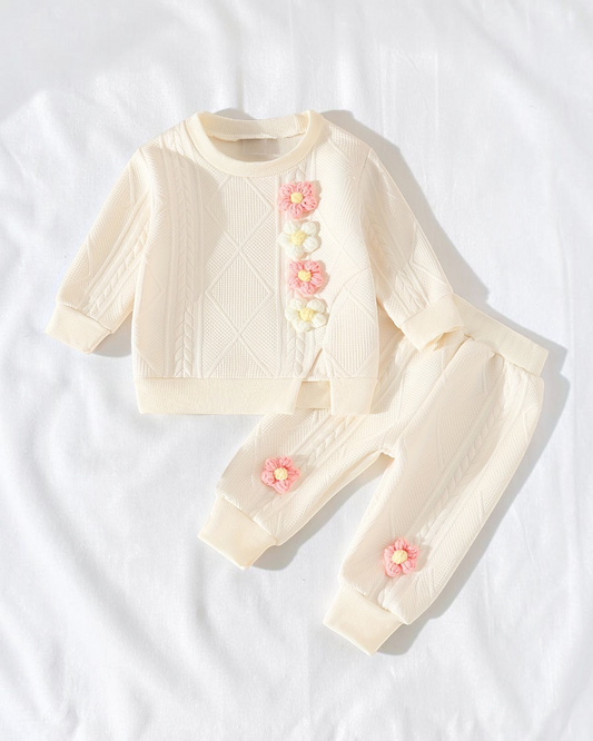Ensemble Le Cocon d'Or pour bébé en maille crème avec fleurs en relief, haut à manches longues et pantalon assorti.