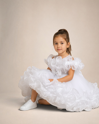 Petite fille portant la robe blanche Royal Bloom de Le Cocon d'Or avec volants, perles et coupe trapèze élégante.