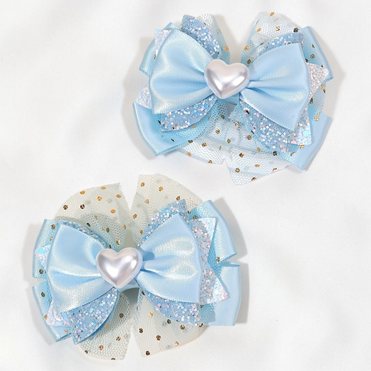 Deux barrettes Le Cocon d'Or bleu clair en forme de nœud avec un cœur nacré et des détails en tulle pailleté.