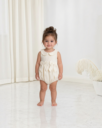 Petite fille portant une combinaison Le Cocon d'Or beige en polyester avec col claudine et nœuds décoratifs