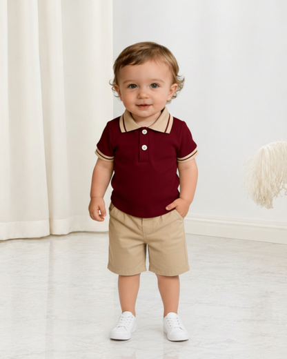 Bébé garçon portant un polo Le Cocon d'Or bordeaux à col beige et un short assorti dans un intérieur lumineux.