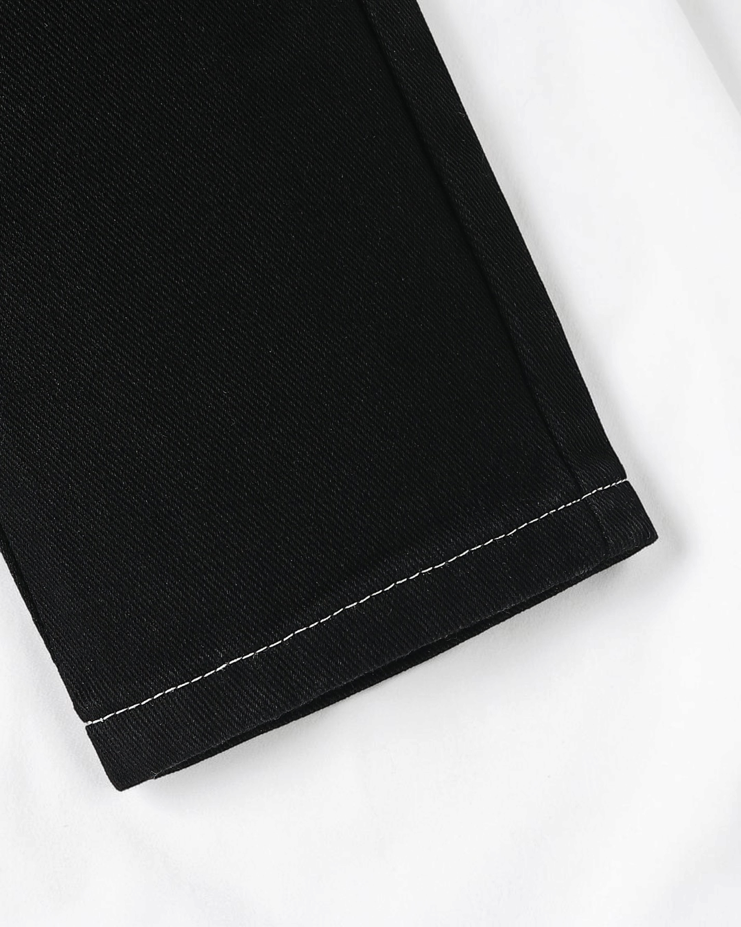 Gros plan sur le bas de jambe d'un jean noir Le Cocon d'Or pour bébé garçon avec surpiqûres blanches contrastantes