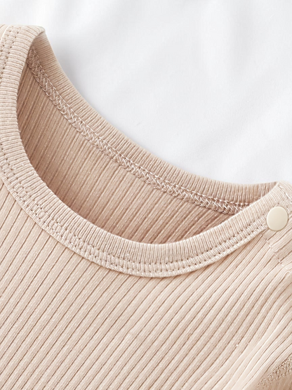 Gros plan sur le col rond côtelé beige d'une combinaison Le Cocon d'Or en coton doux avec bouton pression