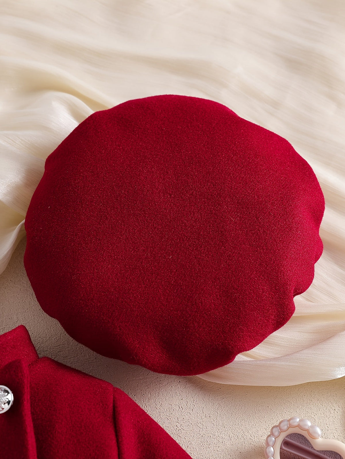 Béret rouge élégant pour bébé fille de la collection Le Cocon d'Or posé sur un tissu crème délicat