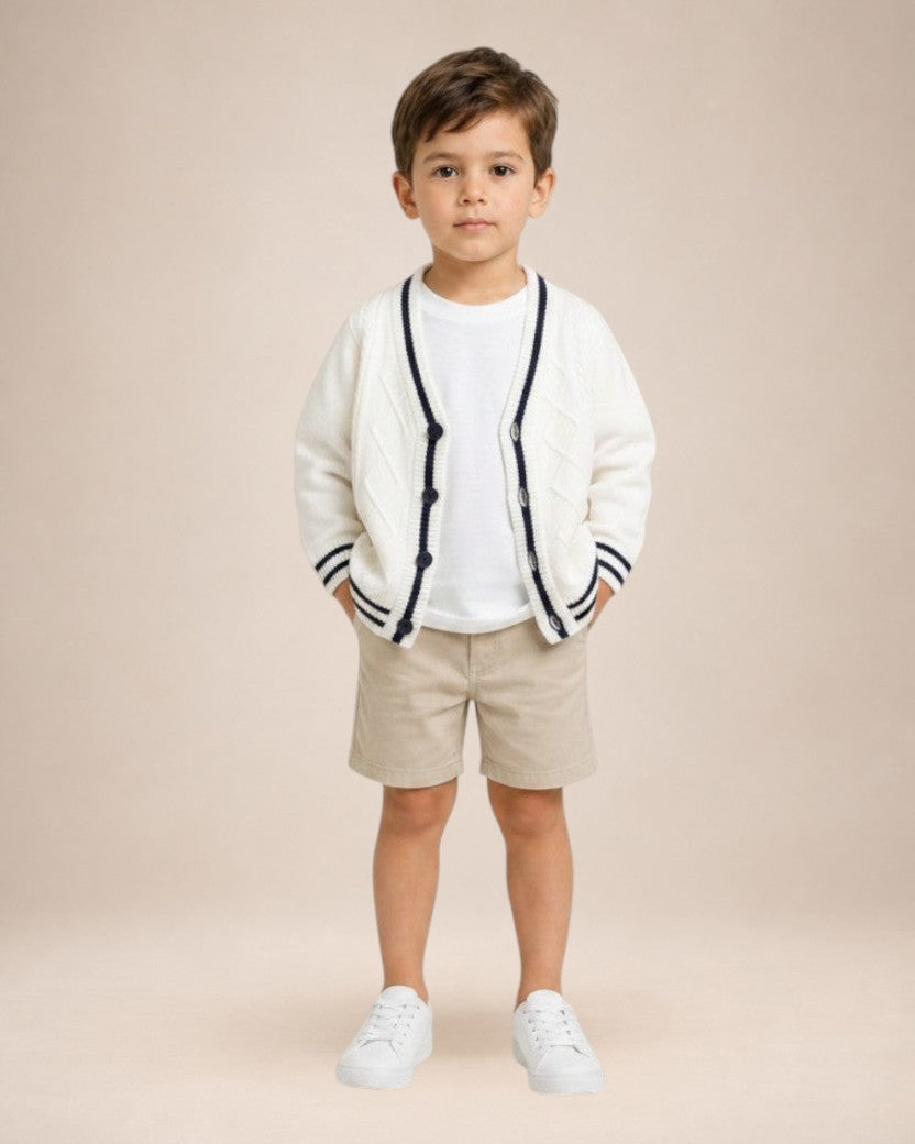 Petit garçon portant un cardigan en maille blanc Le Cocon d'Or avec col en V, bordures contrastées et boutons