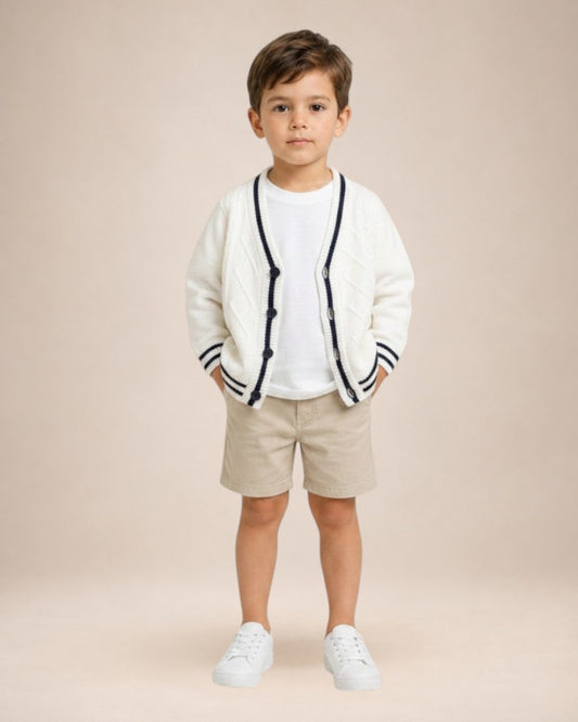 Petit garçon portant un cardigan en maille blanc Le Cocon d'Or avec col en V, bordures contrastées et boutons