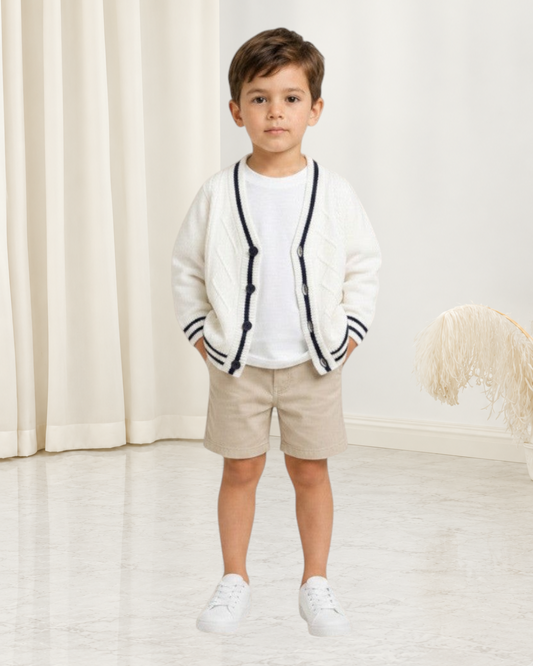 Petit garçon portant un cardigan en maille blanc Le Cocon d'Or avec col en V, bordures contrastées et boutons
