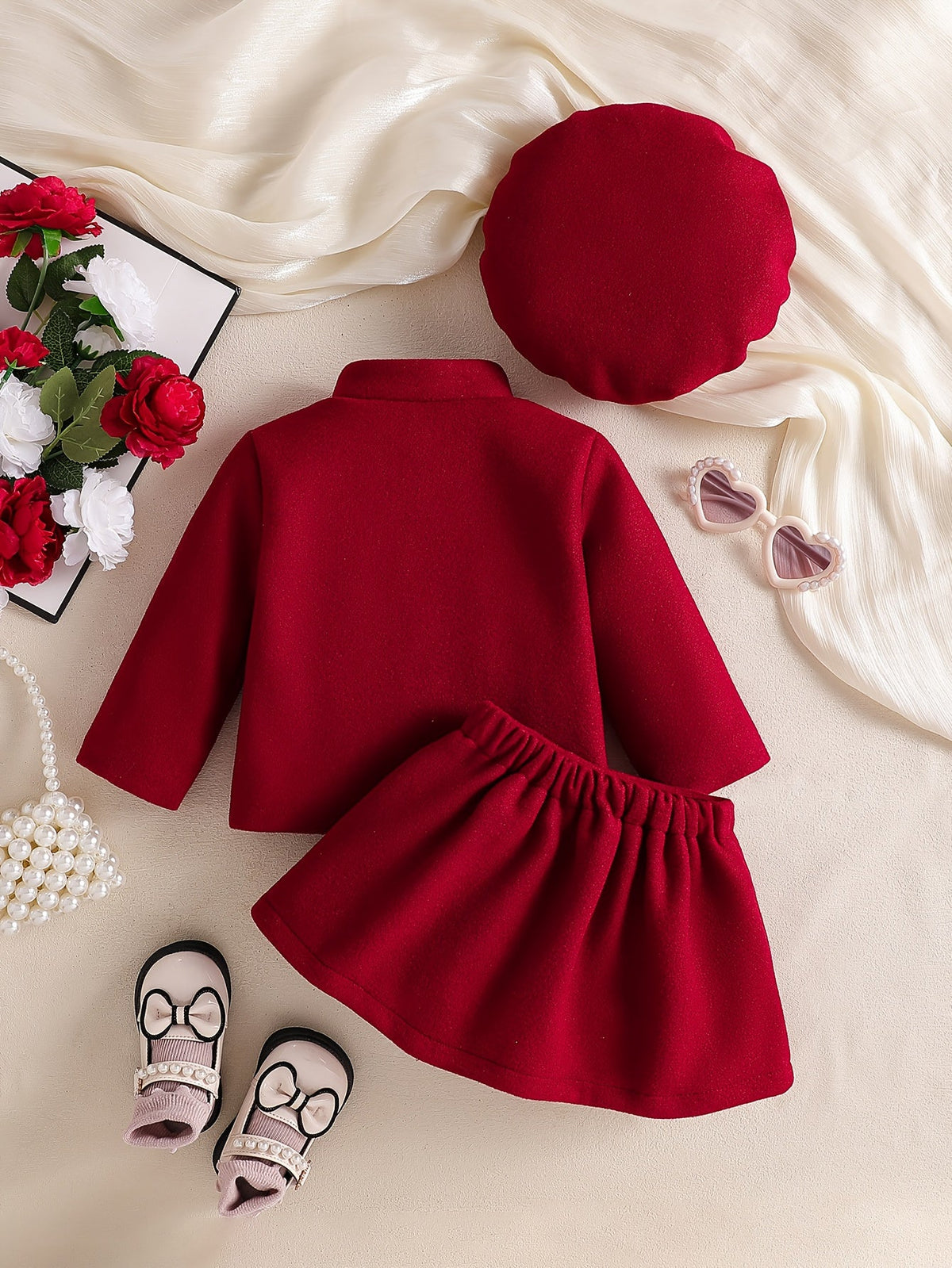 Ensemble Le Cocon d'Or rouge pour bébé fille avec robe, béret, fleurs et accessoires sur fond crème