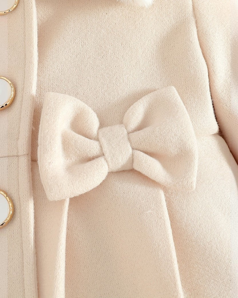 Gros plan sur le manteau Victoria Le Cocon d'Or beige avec un nœud décoratif et des boutons dorés élégants