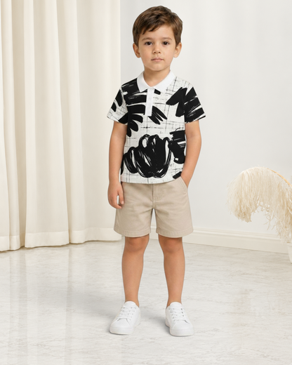 Jeune garçon portant un polo Le Cocon d'Or à motif abstrait noir et blanc avec col classique et short beige