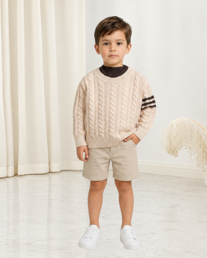 Jeune garçon portant un pull en maille torsadée Le Cocon d'Or beige avec détails rayés sur les manches