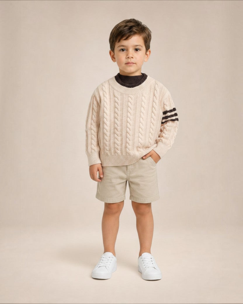 Jeune garçon portant un pull en maille torsadée Le Cocon d'Or beige avec détails rayés sur les manches