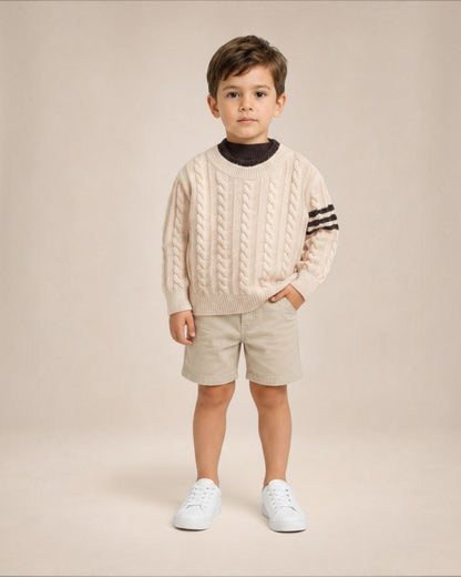 Jeune garçon portant un pull en maille torsadée Le Cocon d'Or beige avec détails rayés sur les manches
