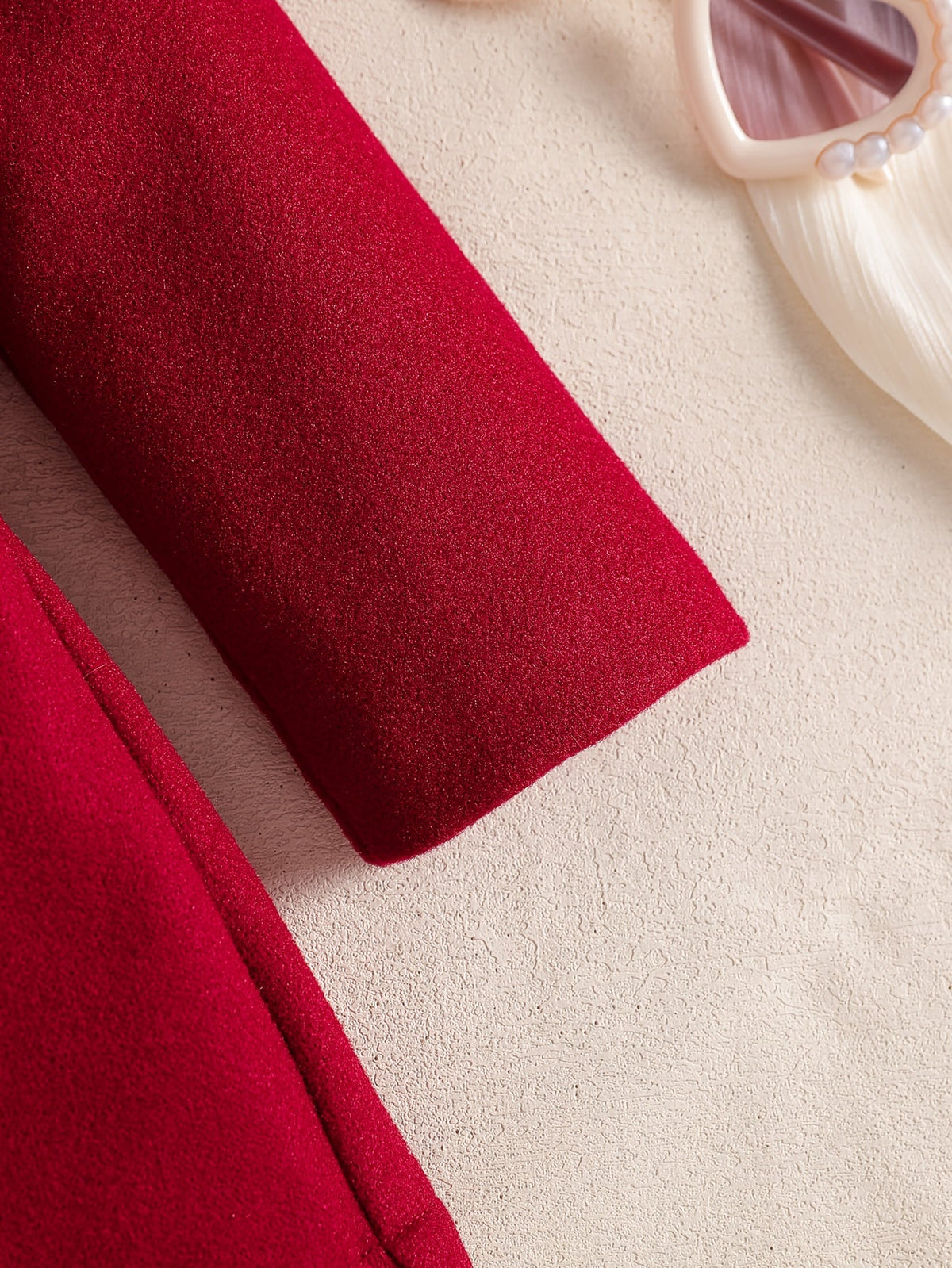 Gros plan sur la manche rouge en maille extensible de la robe Le Cocon d'Or avec des lunettes de soleil à perles