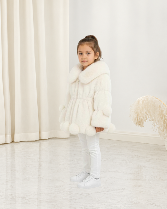 Jeune fille portant une veste en polaire blanche Le Cocon d'Or avec col à revers et détails à pompons